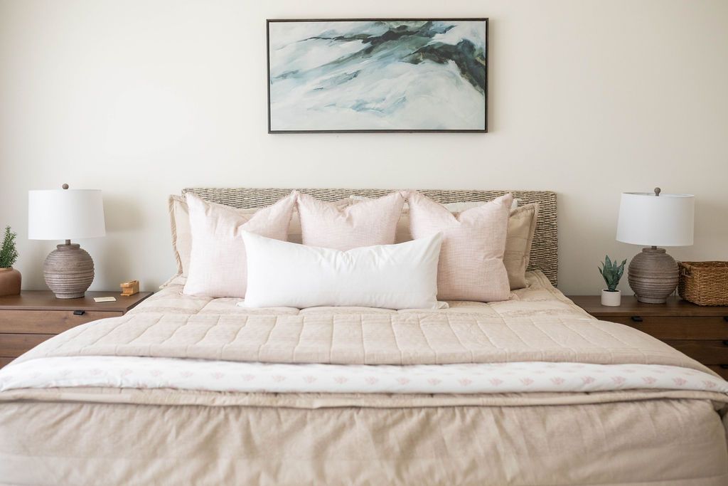 A bed made with tan faded stripes zipper bedding and an assortment of neutral and light pink pillows and blankets.