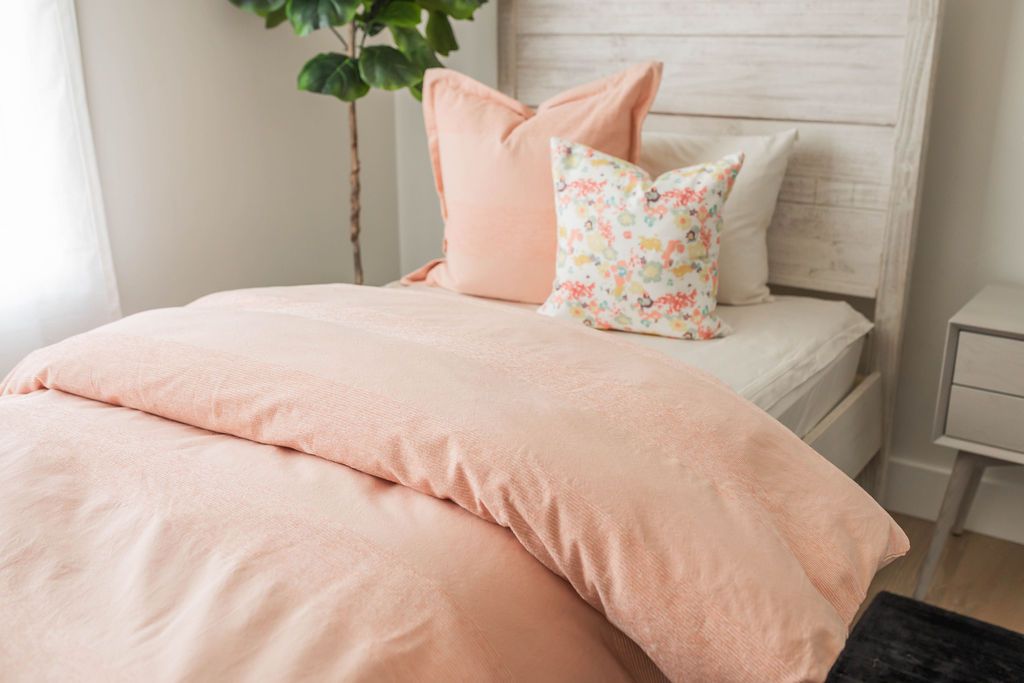 A bed made with white zipper sheets and a peach zipper duvet partially folded half way down the bed and adorned with matching large and multicolor floral pillows.