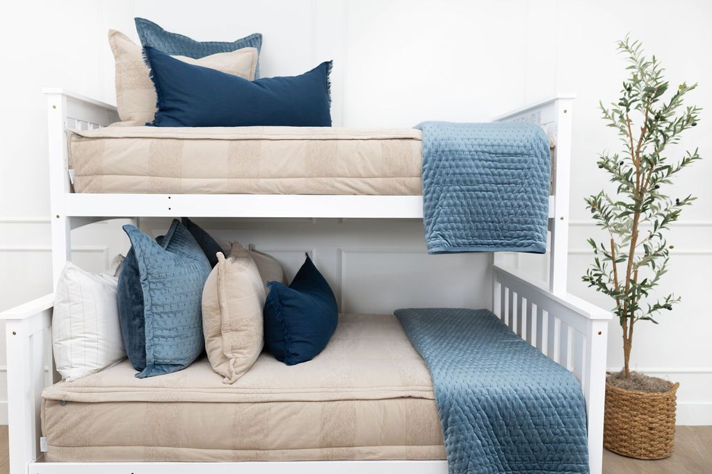 A standard bunk bed with both bunks made with tan zipper bedding and neutral and blue velvet pillows and blankets.