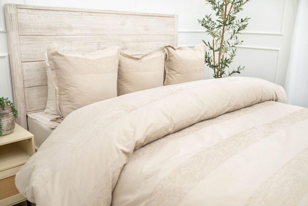 A side view of a bed made with a tan zipper duvet folded partially down the bed and adorned with neutral large matching pillows.