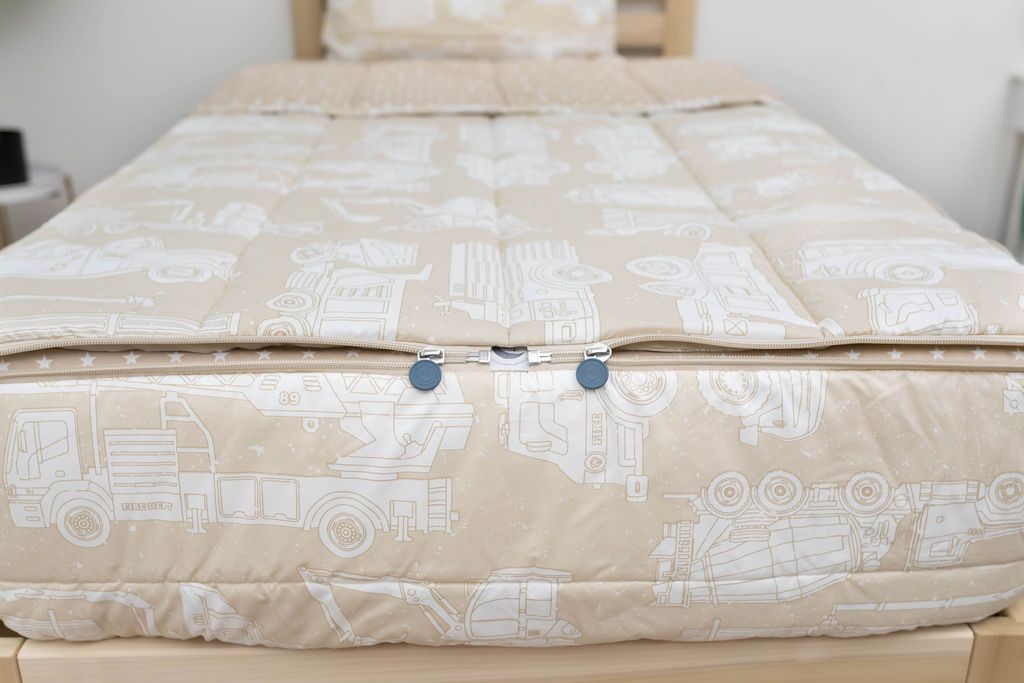 The foot of a bed made with light tan cars kids zipper bedding showing where the two zippers are located.