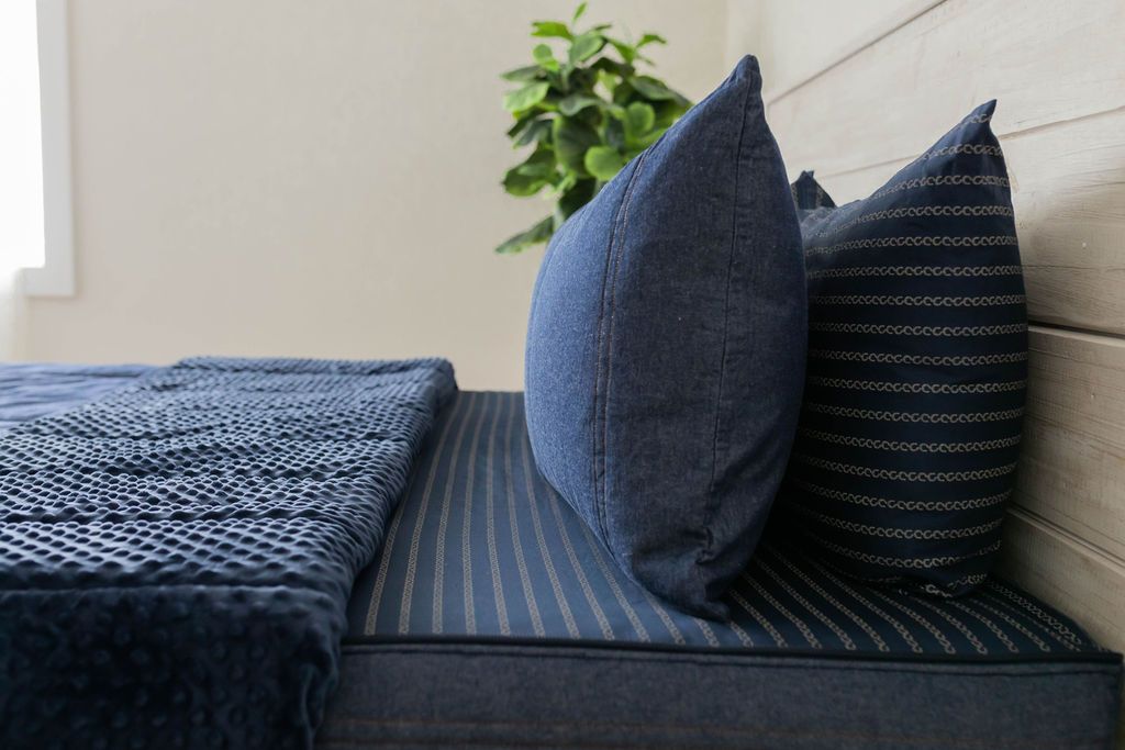 A side view of a bed with dark blue pillowcases on a denim blue unzipped zipper bedding. 