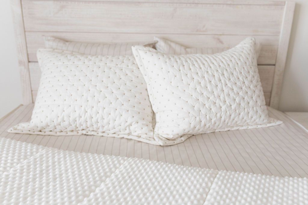 A bed made with cream embroidered zipper bedding with the comforter pulled back and pillows on top of the bed.