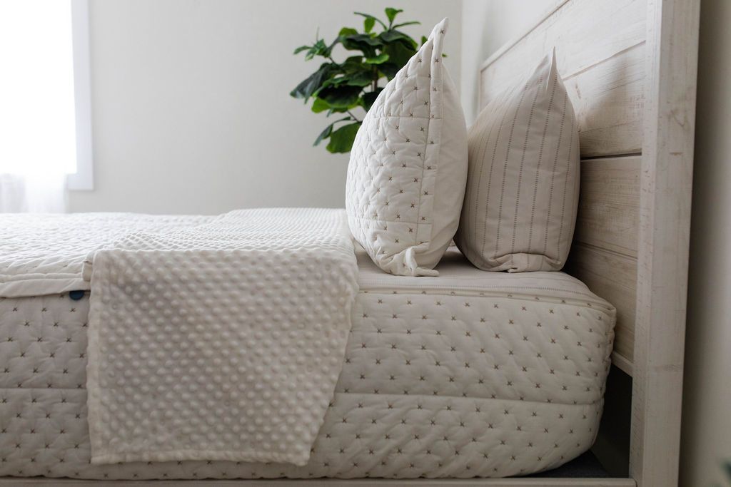 A side view of a bed made with cream embroidered zipper bedding with the top unzipped partially down the bed showing the minky interior side panel. 