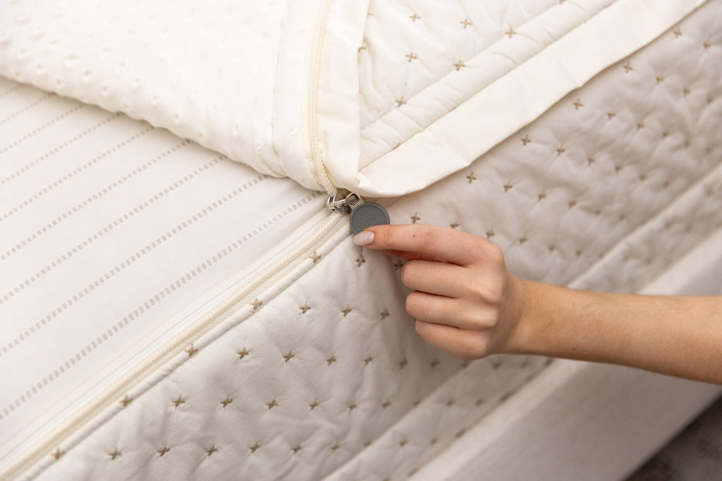 A close up view of a bed made with cream embroidered zipper bedding with the bed slightly unzipped to reveal the minky comforter and the light tan and cream striped pattern bottom cotton lining.