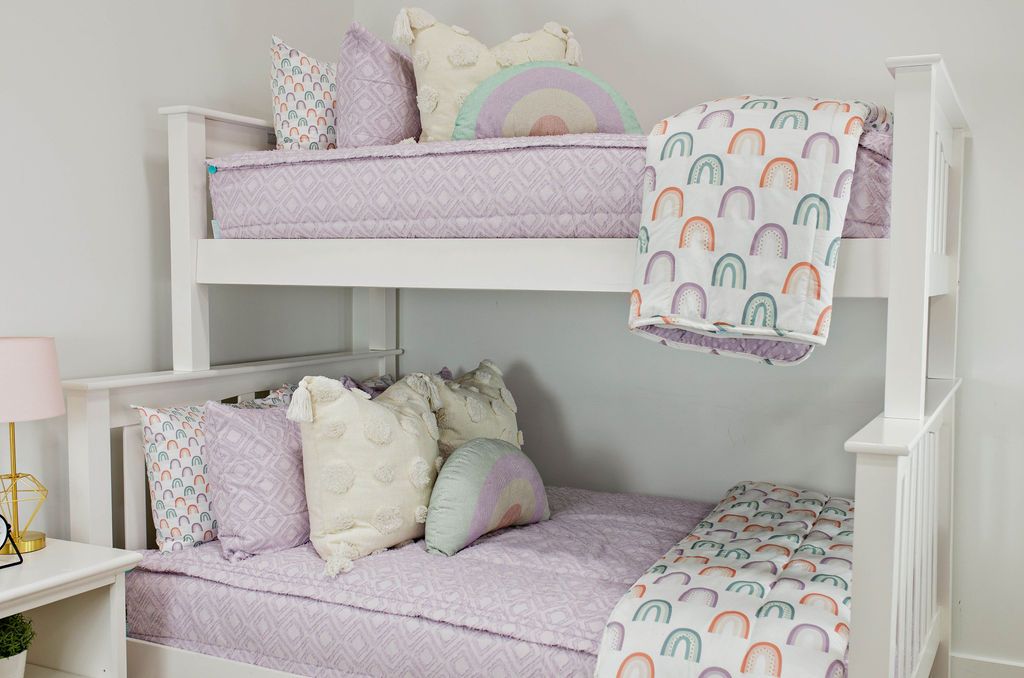 A standard bunk bed with both bunks made with light purple textured zipper bedding and neutral and pastel rainbow pattern pillows and blankets.