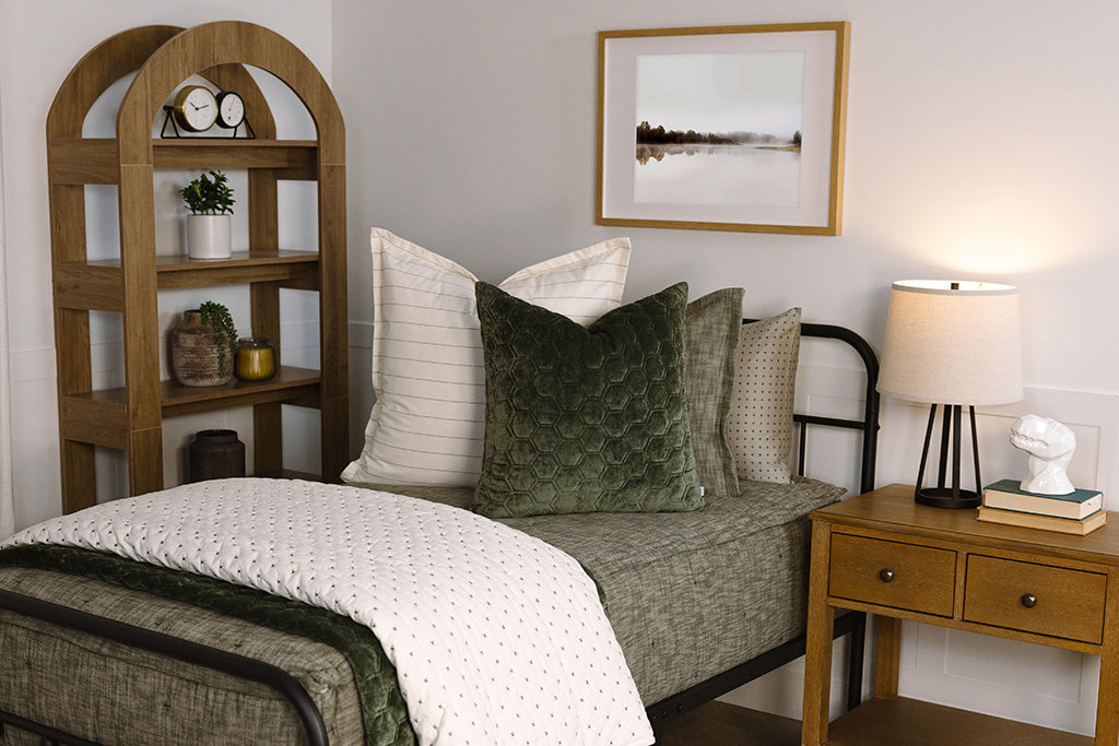 A twin bed made with deep emerald green zipper bedding and white striped and green pillows and blankets.