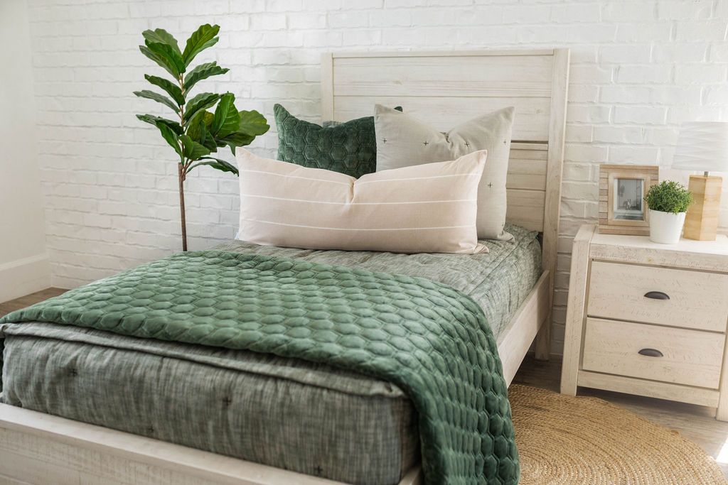 A twin bed made with dark green zipper bedding and neutral and velvet green pillows and blanket.