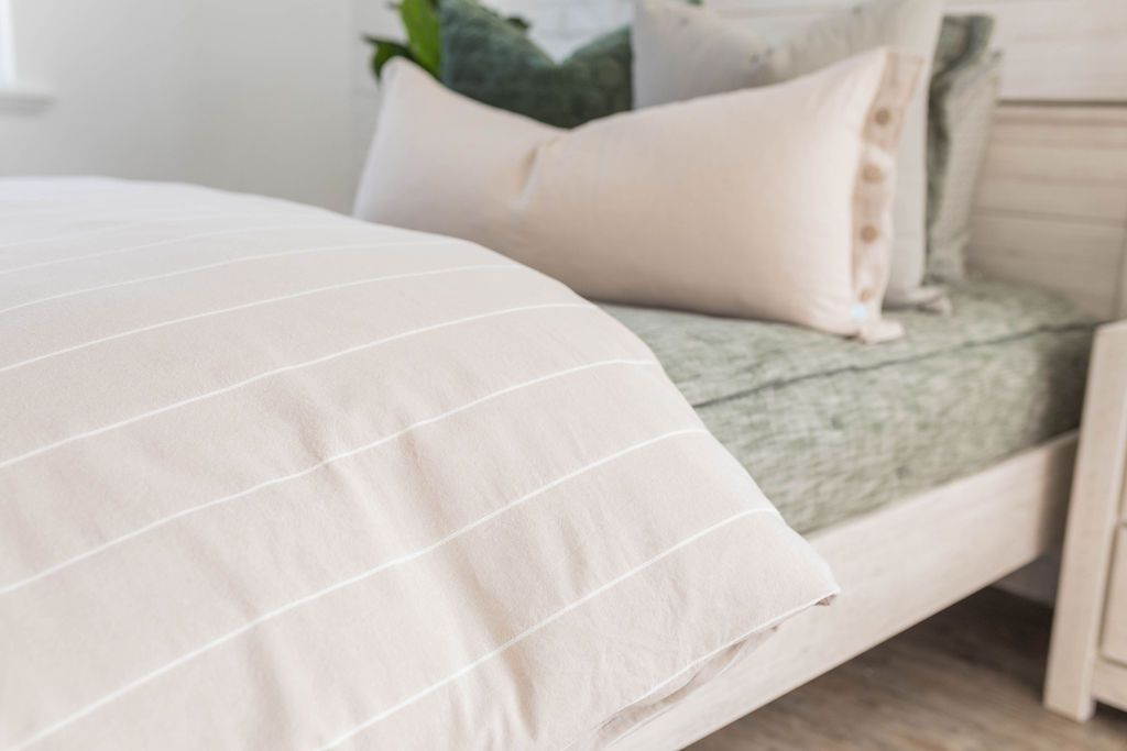 A side view of a bed made with dark emerald green zipper bedding and a tan and white striped zipper duvet folded half way down the bed and adorned with neutral and green pillows.
