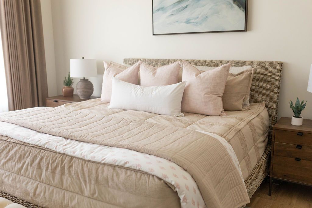 A bed made with tan zipper bedding and an assortment of neutral and light pink throw pillows and blankets.